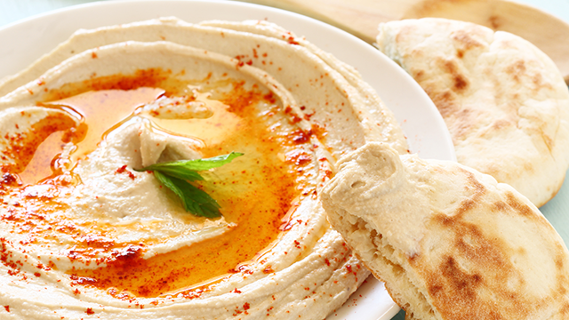 A bowl of hummus with pita wedges on the side.