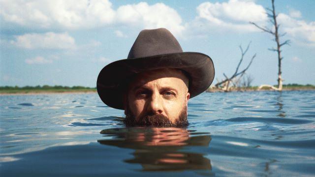 马蒂·布什戴着牛仔帽从湖中浮出水面. 他被淹没在他的胡子和面对观众.